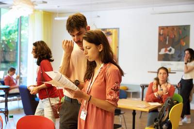 Eine junge Frau und ein junger Mann betrachten gemeinsam das Tagesprogramm des Grossen Schnuppertags. Der Mann blickt über die Schulter der Frau. Im Hintergrund ist die Lobby der Heilpraktikerschule Luzern zu sehen. 
