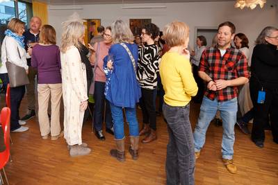 Gruppe von Menschen in einem Raum mit Holzboden, die in kleinen Gruppen stehen und sich unterhalten.