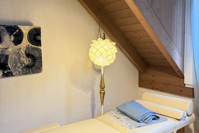 Behandlungsraum mit Massageliege unter einer schrägen Holzbalkendecke.