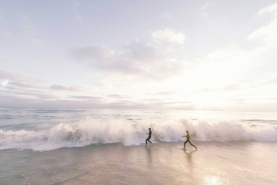 Foto von zwei Menschen, die bald von einer Welle etwas getaucht werden. Foto: Unsplash