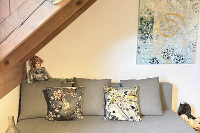 Graues Sofa mit zwei gemusterten Kissen unter einer Dachschräge mit Holzverkleidung.