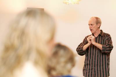 Ein Mann mit gestreiftem Hemd steht vor einer Gruppe und hält die Hände vor der Brust zusammen.