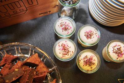 Glasgefässe mit weisser Creme und braun-rosa Streuseln neben einem Teller mit Brownies. 