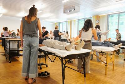 In einem Schulzimmer üben TeilnehmerInnen paarweise an Behandlungsliegen.