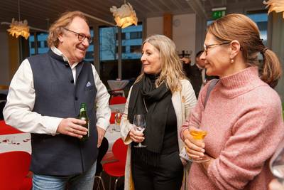 Drei Personen stehen in einem Raum mit roten Stühlen und halten Getränke in der Hand.