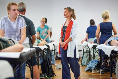 Regula steht in einem Schulzimmer zwischen mehreren Behandlungsliegen, an denen TeilnehmerInnen paarweise üben.