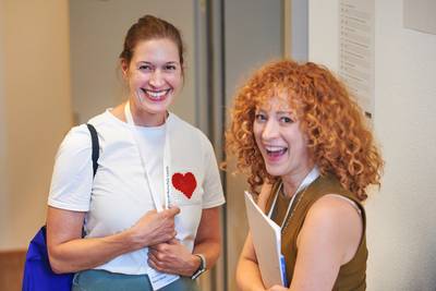 Zwei Besucherinnen stehen nebeneinander, schauen in die Kamera und lachen.