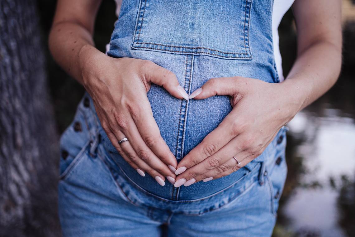 Bild einer Schwangeren im Jeansanzug, die Schwangere bildet mit ihren Händen ein Herz auf ihrem Bauch; das Bild ist von Pixabay.